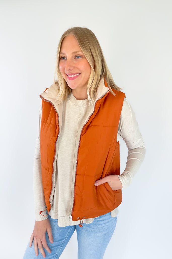This stylish Beige + Orange Reversible Puff Vest is a great way to stay warm without sacrificing your sense of style. It comes in a beige and orange color that's eye-catching. It features a zip-up front, side pockets, and an adjustable drawstring at the bottom for a perfect fit.