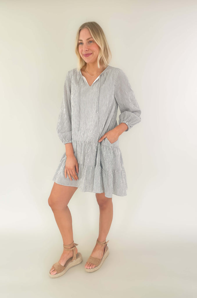 Freshen up your wardrobe with the black and white stripe By the Bay Tiered Dress! Featuring a lightweight fabric, long sleeves, side pockets and tassel ties, this timeless look is a fashionable must-have! 