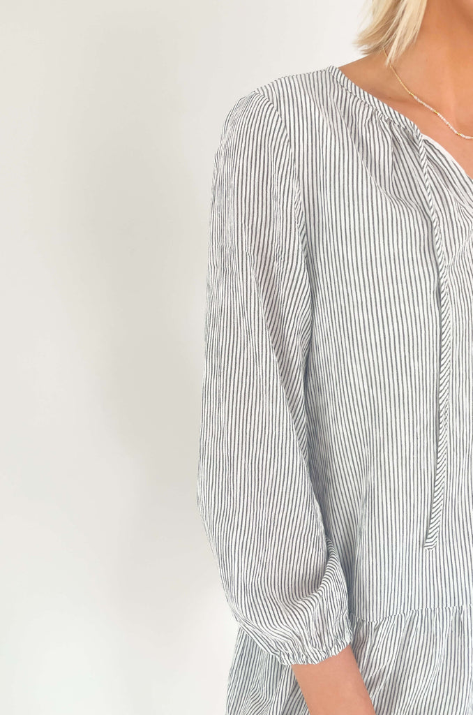 Freshen up your wardrobe with the black and white stripe By the Bay Tiered Dress! Featuring a lightweight fabric, long sleeves, side pockets and tassel ties, this timeless look is a fashionable must-have! 