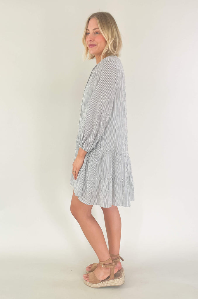 Freshen up your wardrobe with the black and white stripe By the Bay Tiered Dress! Featuring a lightweight fabric, long sleeves, side pockets and tassel ties, this timeless look is a fashionable must-have! 