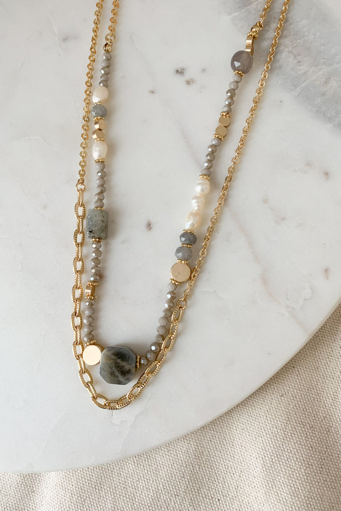This Grey Beaded Layer Necklace makes a perfect accent to any outfit! It features multiple layers, one of them being a classic gold chain, and the other features gorgeous mixed beads. Some of the beads are grey, gold, pearlescent, or large stones. The necklace is 15 1/2" and has a 3" extender.