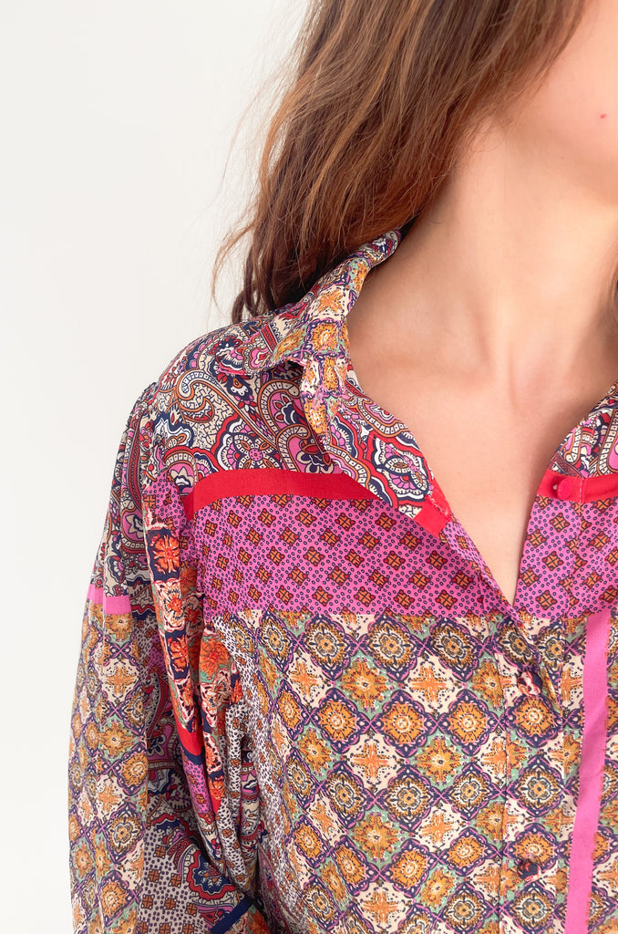 This Hot Pink & Red Boho Long Sleeve Blouse has a lightweight sheer material and features a stylish collar and cinched wrists for a sleek work look! The stylish print features pops of red, magenta, mustard, and green.