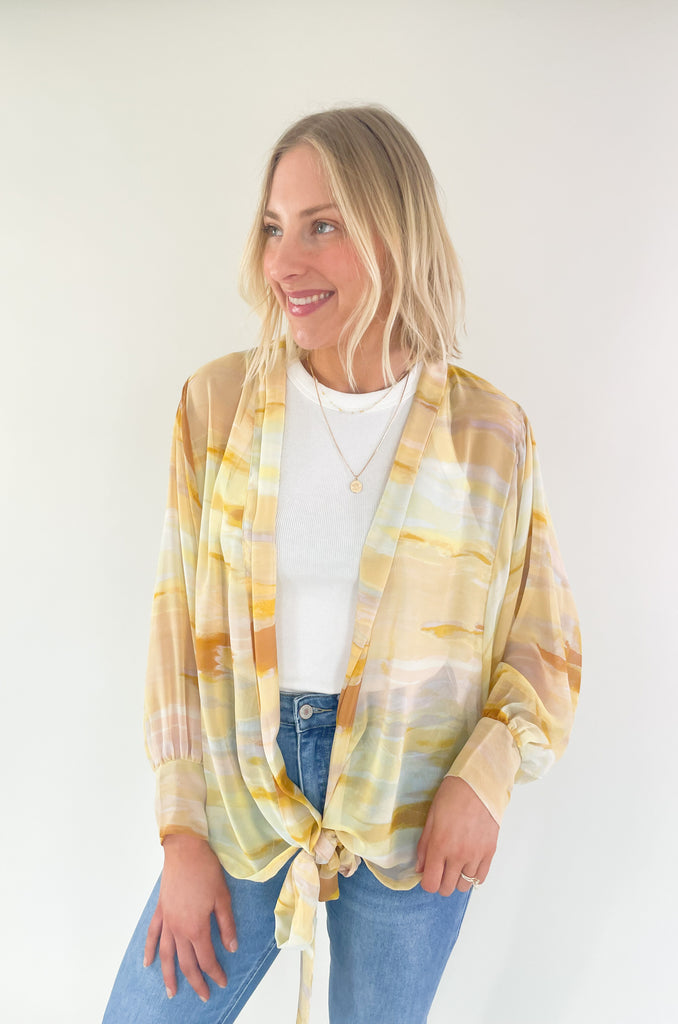Brighten up your closet with the Madrid Relaxed Kimono. This stylish piece features a beautiful yellow, peach, and white watercolor print, balloon sleeves, and a flattering adjustable tie in the front. It's perfect for adding a splash of color to any outfit.