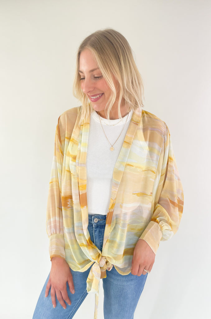 Brighten up your closet with the Madrid Relaxed Kimono. This stylish piece features a beautiful yellow, peach, and white watercolor print, balloon sleeves, and a flattering adjustable tie in the front. It's perfect for adding a splash of color to any outfit.