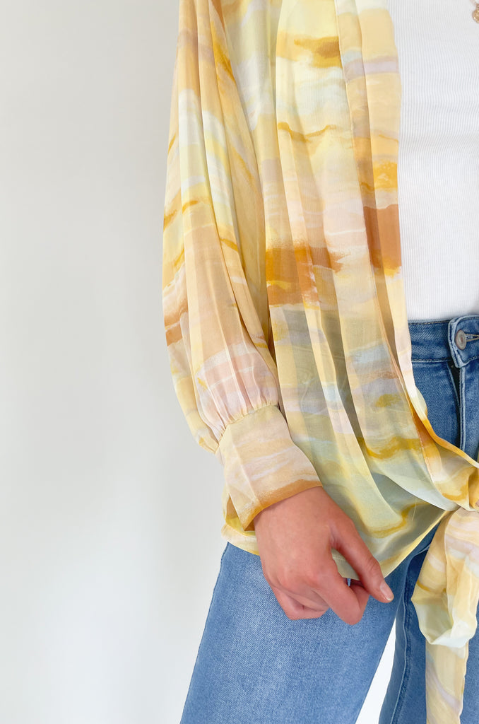 Brighten up your closet with the Madrid Relaxed Kimono. This stylish piece features a beautiful yellow, peach, and white watercolor print, balloon sleeves, and a flattering adjustable tie in the front. It's perfect for adding a splash of color to any outfit.