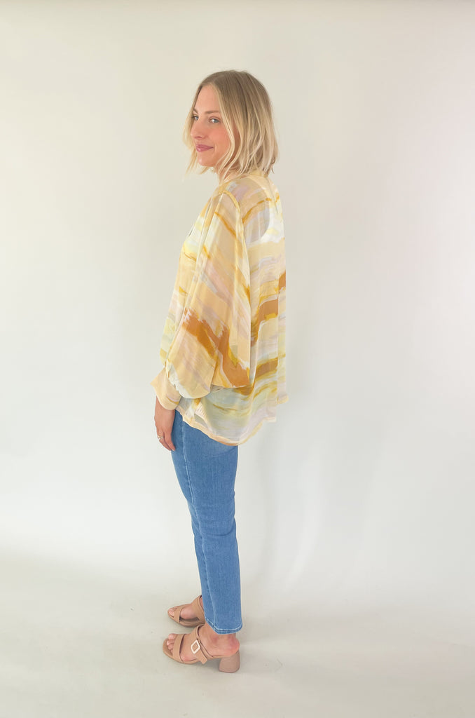 Brighten up your closet with the Madrid Relaxed Kimono. This stylish piece features a beautiful yellow, peach, and white watercolor print, balloon sleeves, and a flattering adjustable tie in the front. It's perfect for adding a splash of color to any outfit.