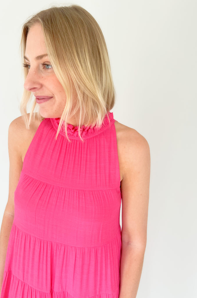 high ruffle neck sleeveless dress with back tie, side pockets, and tiered shape. Available in a bright fuchsia and coral. 