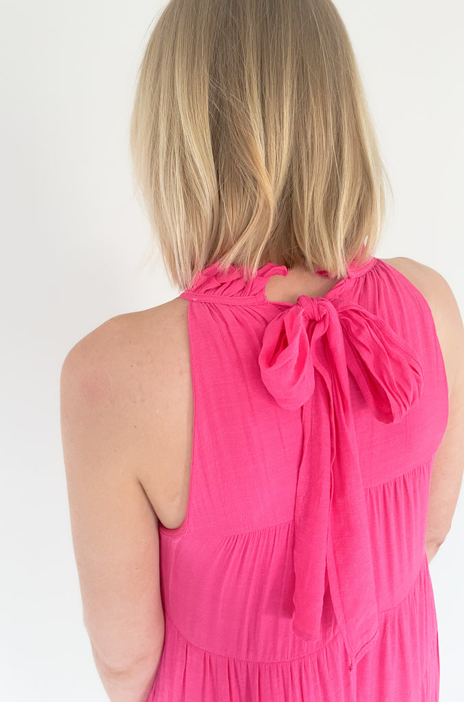 high ruffle neck sleeveless dress with back tie, side pockets, and tiered shape. Available in a bright fuchsia and coral. 