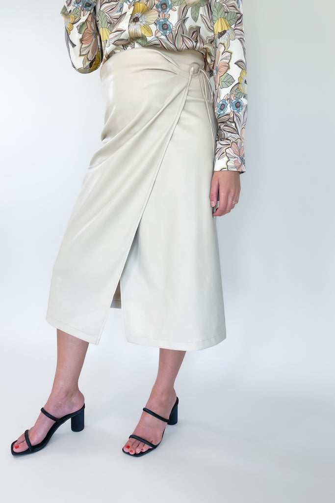 The Sandi Wrap Midi Skirt is a must-have for any fashion lover. It's no secret that skirts are taking the world by storm, especially midi styles like this one. It's crafted from a beige faux leather with a soft fabric lining. The soft inside ensures comfort, while the tassel ties and flattering fit add a stylish touch.