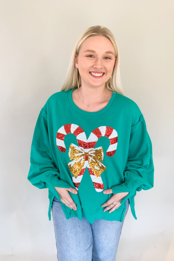 Talk about some holiday fun! This eye-catching green candy cane sequin sweater is so unique and special. Be festive and jolly all season in this bright green round neck sweater with a bold sequin candy cane design on the from. The sleeves have fun slits and the sides are slit as well, helping the style lay well over jeans and leggings. 