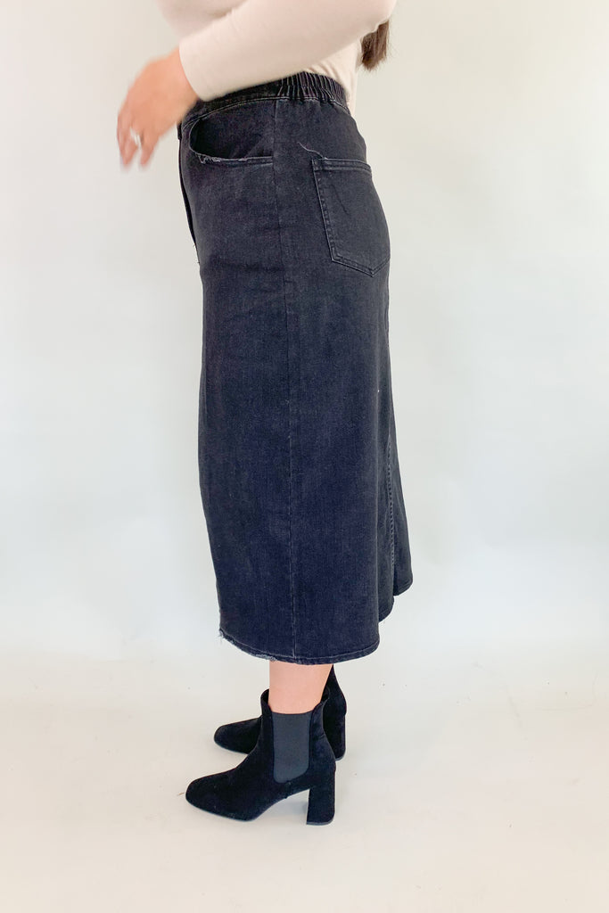 The Vintage Wash Black Denim Midi Skirt is super trendy, but very comfortable for an all denim skirt. The elastic back and lighter weight fabric makes this skirt a go-to for fall! We love the washed black color, front slit, and raw hem, giving this style an edgy look. 