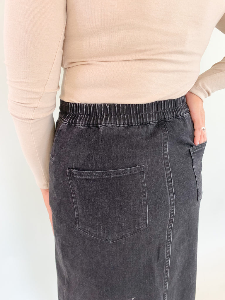The Vintage Wash Black Denim Midi Skirt is super trendy, but very comfortable for an all denim skirt. The elastic back and lighter weight fabric makes this skirt a go-to for fall! We love the washed black color, front slit, and raw hem, giving this style an edgy look. 
