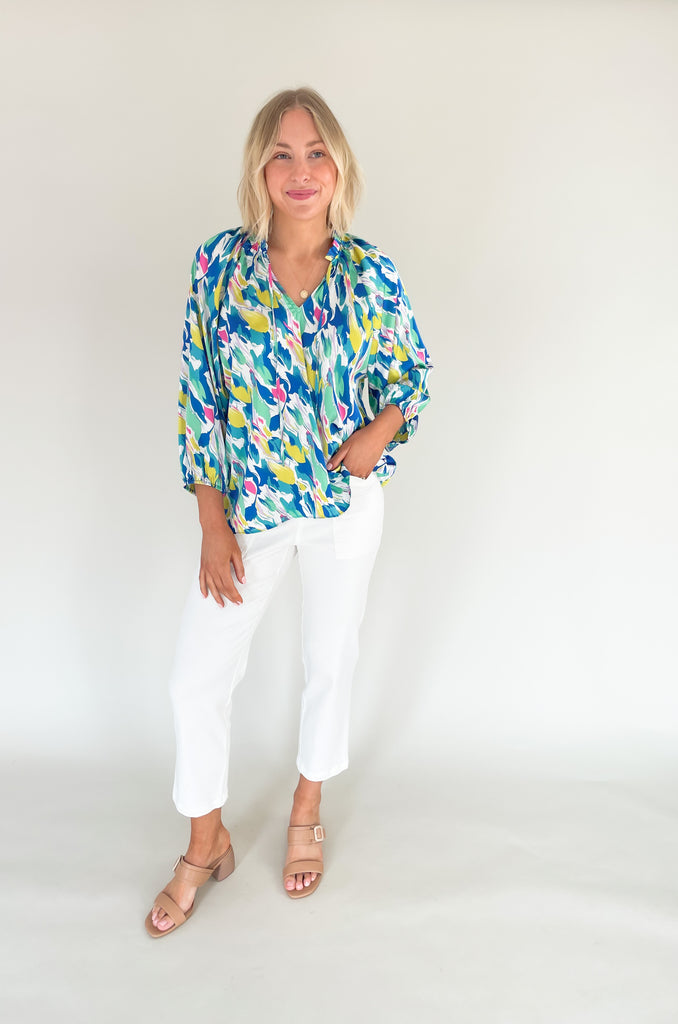 Long sleeve blouse with pops of vibrant blues, yellow, and pinks, flowy with balloon sleeve, lightweight silky feel, V-neck with a tie detailing and pleated neckline