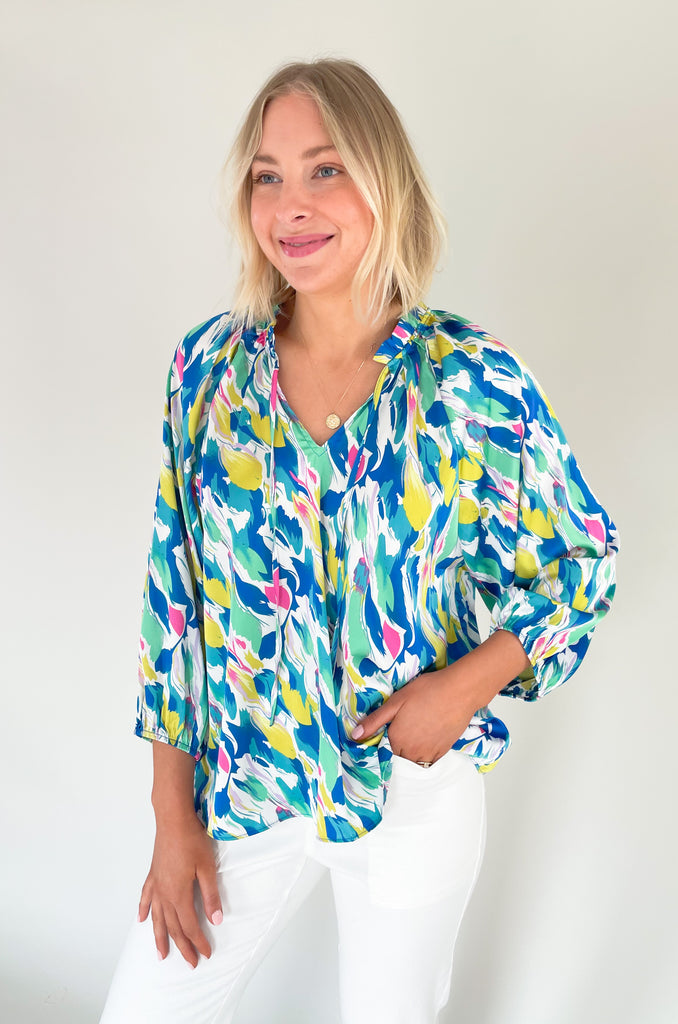 Long sleeve blouse with pops of vibrant blues, yellow, and pinks, flowy with balloon sleeve, lightweight silky feel, V-neck with a tie detailing and pleated neckline