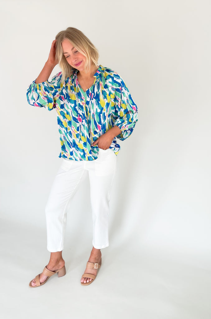 Long sleeve blouse with pops of vibrant blues, yellow, and pinks, flowy with balloon sleeve, lightweight silky feel, V-neck with a tie detailing and pleated neckline