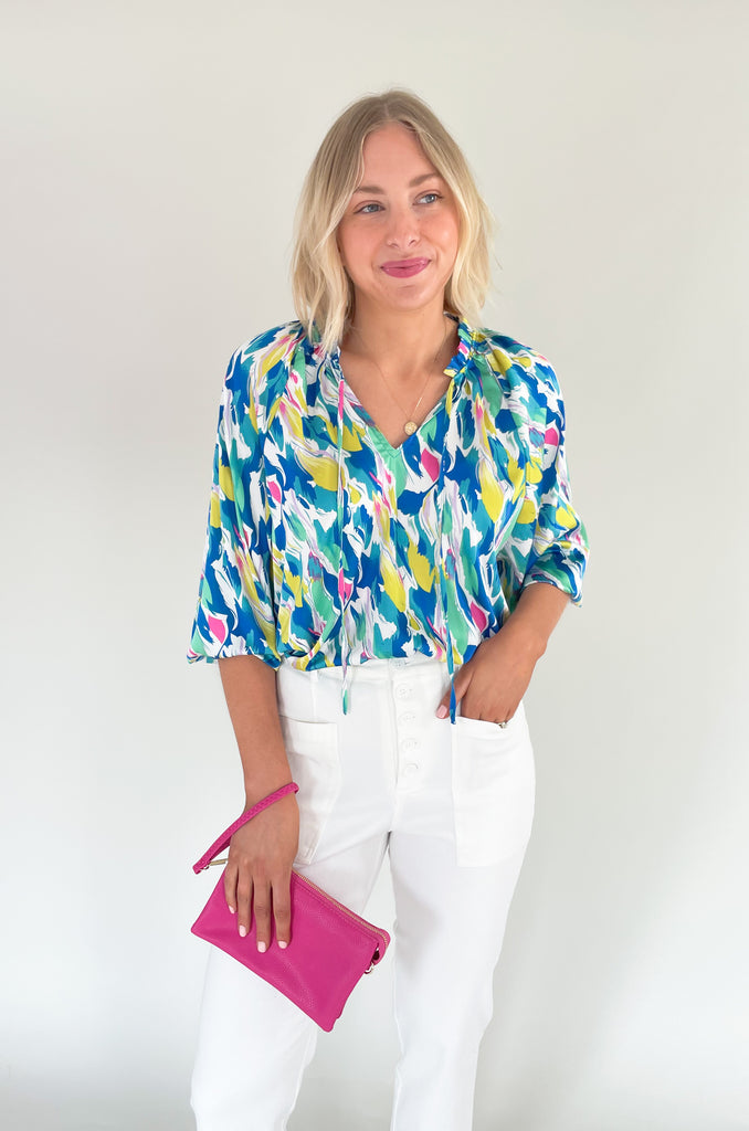 Long sleeve blouse with pops of vibrant blues, yellow, and pinks, flowy with balloon sleeve, lightweight silky feel, V-neck with a tie detailing and pleated neckline