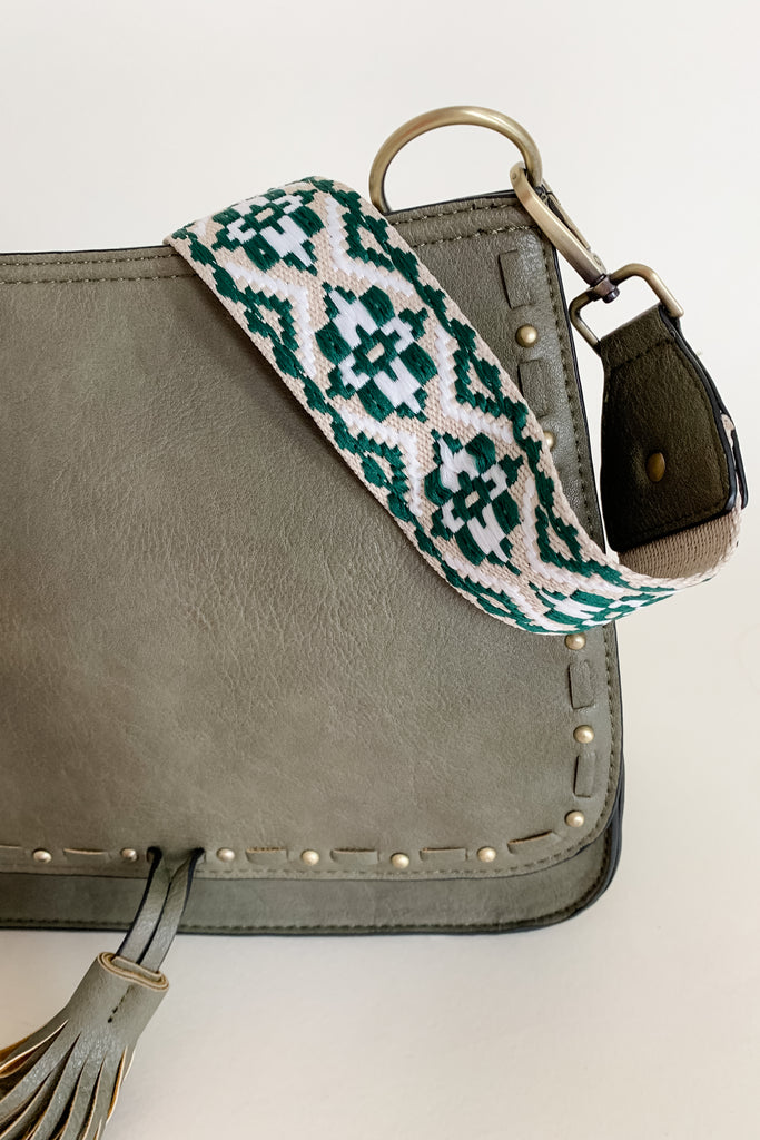 The Baylor Flapover Tassel Crossbody comes in three great colors: Brown, Teal, and Olive. It's a square shape that tapers at the top. Because of the unique shape, it fits comfortably right at the hip. Each bag comes with an exclusive guitar strap. On the flap, there are hammered metallic dots that embroider it. There is also a unique woven stitching followed by a tassel. This bag is right on trend this season, the perfect size, and all vegan leather! 