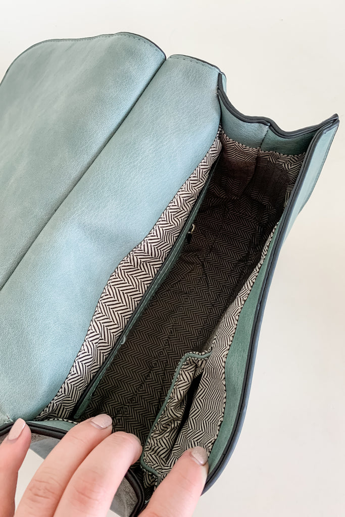 The Baylor Flapover Tassel Crossbody comes in three great colors: Brown, Teal, and Olive. It's a square shape that tapers at the top. Because of the unique shape, it fits comfortably right at the hip. Each bag comes with an exclusive guitar strap. On the flap, there are hammered metallic dots that embroider it. There is also a unique woven stitching followed by a tassel. This bag is right on trend this season, the perfect size, and all vegan leather! 