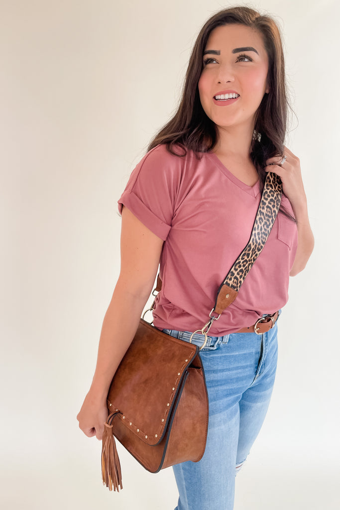 The Baylor Flapover Tassel Crossbody comes in three great colors: Brown, Teal, and Olive. It's a square shape that tapers at the top. Because of the unique shape, it fits comfortably right at the hip. Each bag comes with an exclusive guitar strap. On the flap, there are hammered metallic dots that embroider it. There is also a unique woven stitching followed by a tassel. This bag is right on trend this season, the perfect size, and all vegan leather! 