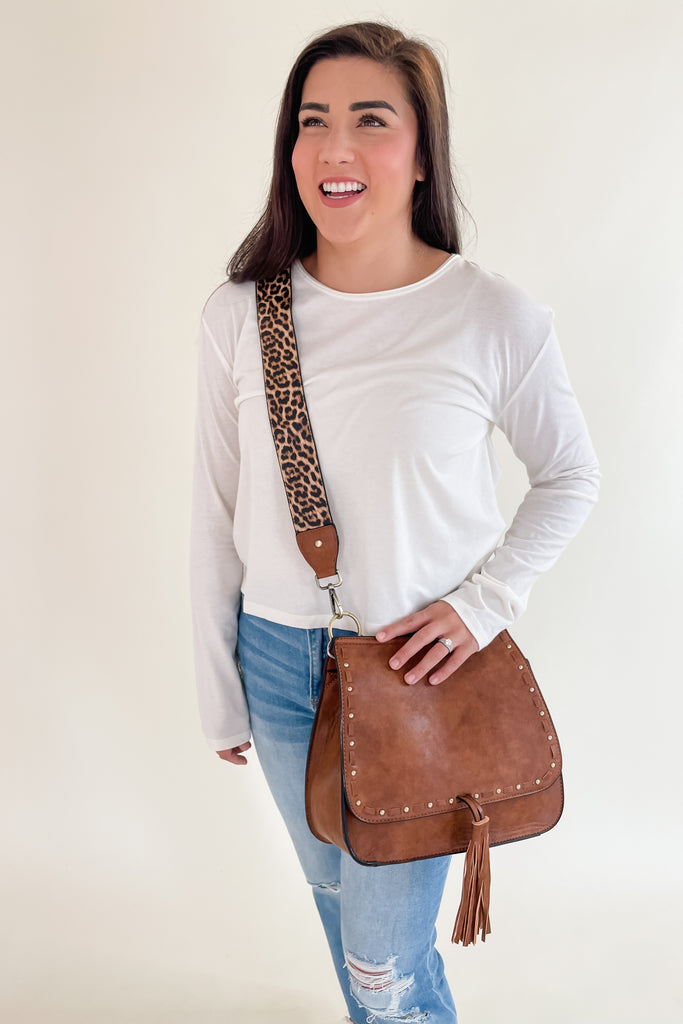 The Baylor Flapover Tassel Crossbody comes in three great colors: Brown, Teal, and Olive. It's a square shape that tapers at the top. Because of the unique shape, it fits comfortably right at the hip. Each bag comes with an exclusive guitar strap. On the flap, there are hammered metallic dots that embroider it. There is also a unique woven stitching followed by a tassel. This bag is right on trend this season, the perfect size, and all vegan leather! 