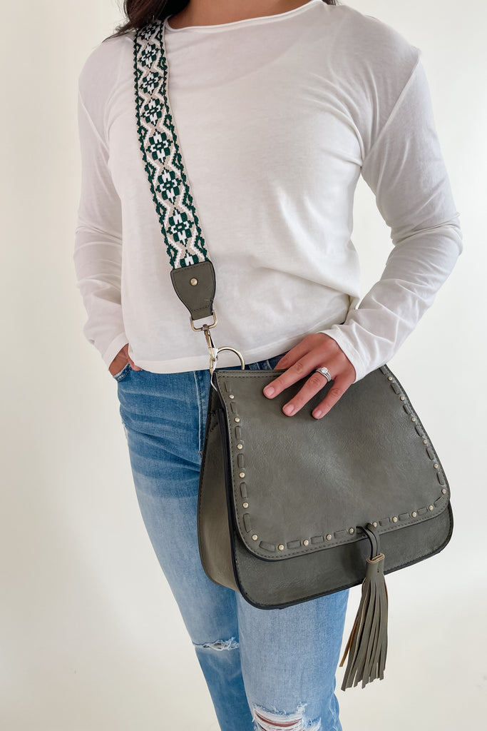 The Baylor Flapover Tassel Crossbody comes in three great colors: Brown, Teal, and Olive. It's a square shape that tapers at the top. Because of the unique shape, it fits comfortably right at the hip. Each bag comes with an exclusive guitar strap. On the flap, there are hammered metallic dots that embroider it. There is also a unique woven stitching followed by a tassel. This bag is right on trend this season, the perfect size, and all vegan leather! 