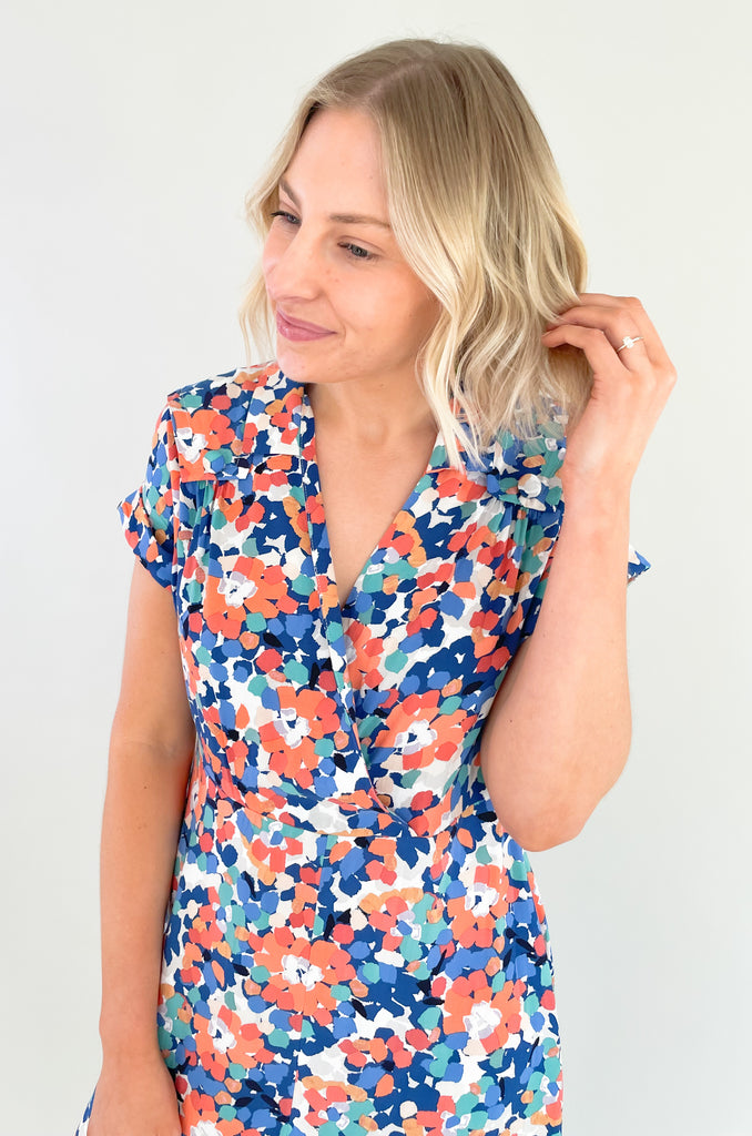 This stunning blue and coral floral print mini dress is designed to make you feel feminine, stylish, and confident. This dress features a flattering V-neckline that and wrap silhouette. It drapes beautifully over your body, creating a flattering and flowy fit. It has a collar detail, pleating around the neckline too. Plus, the colors are just so fun!